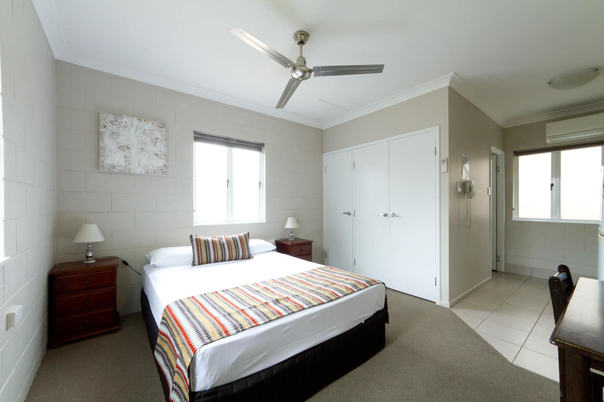 A bedroom with a bed, a ceiling fan, a window, a wardrobe, and a nightstand.