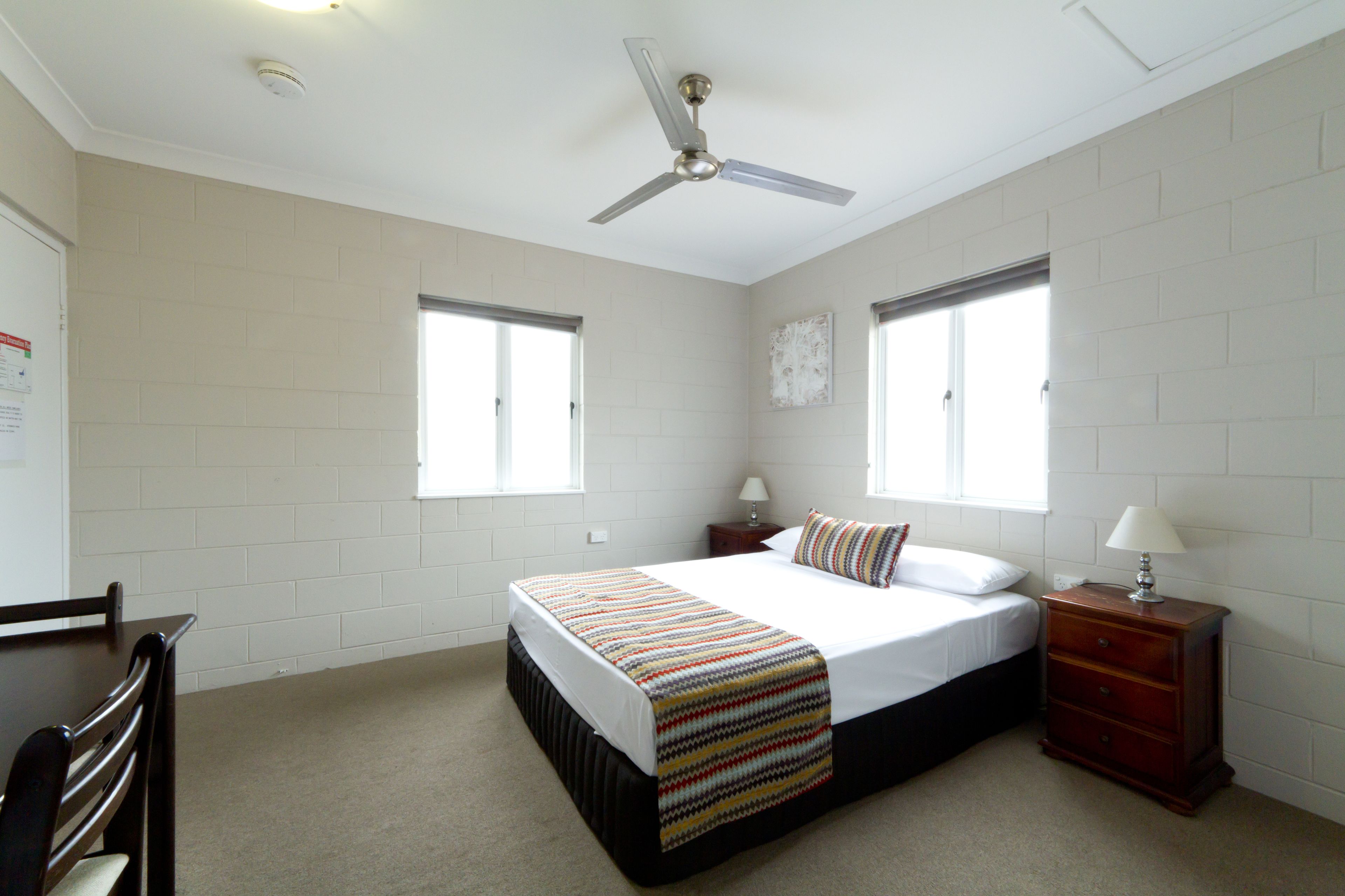 A bedroom with a bed, nightstands, a wooden dresser, and a ceiling fan.