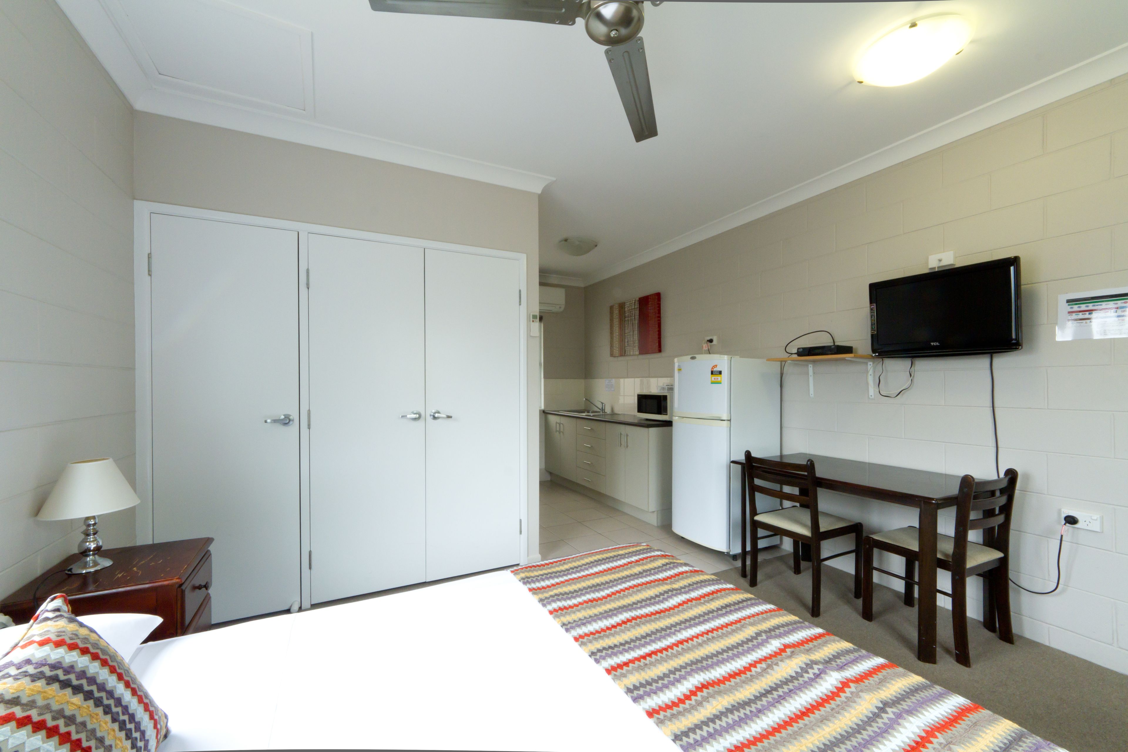 A hotel room with a bed, a desk, a chair, a television, a microwave, and a refrigerator.