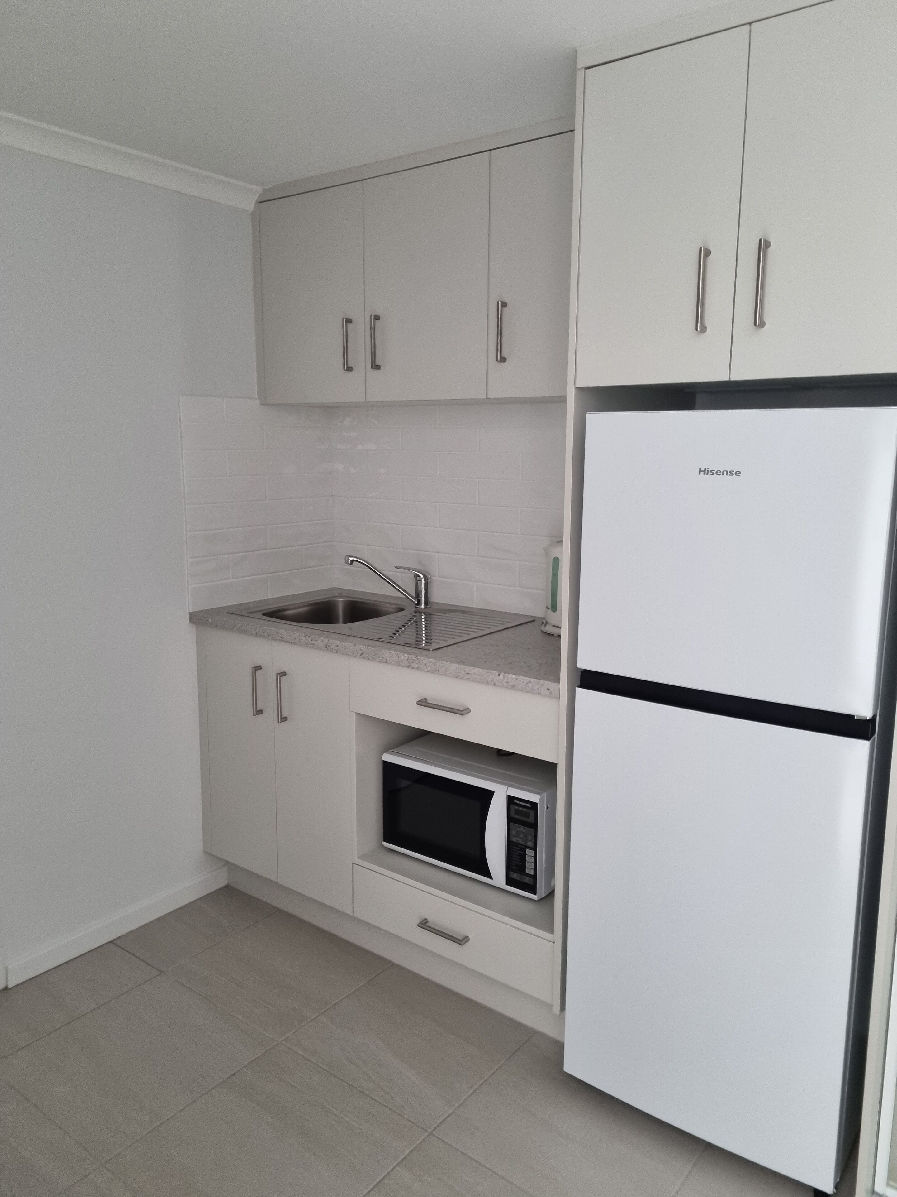 A modern kitchen with white cabinetry, a stainless steel sink, a built-in microwave, and a Hisense refrigerator.