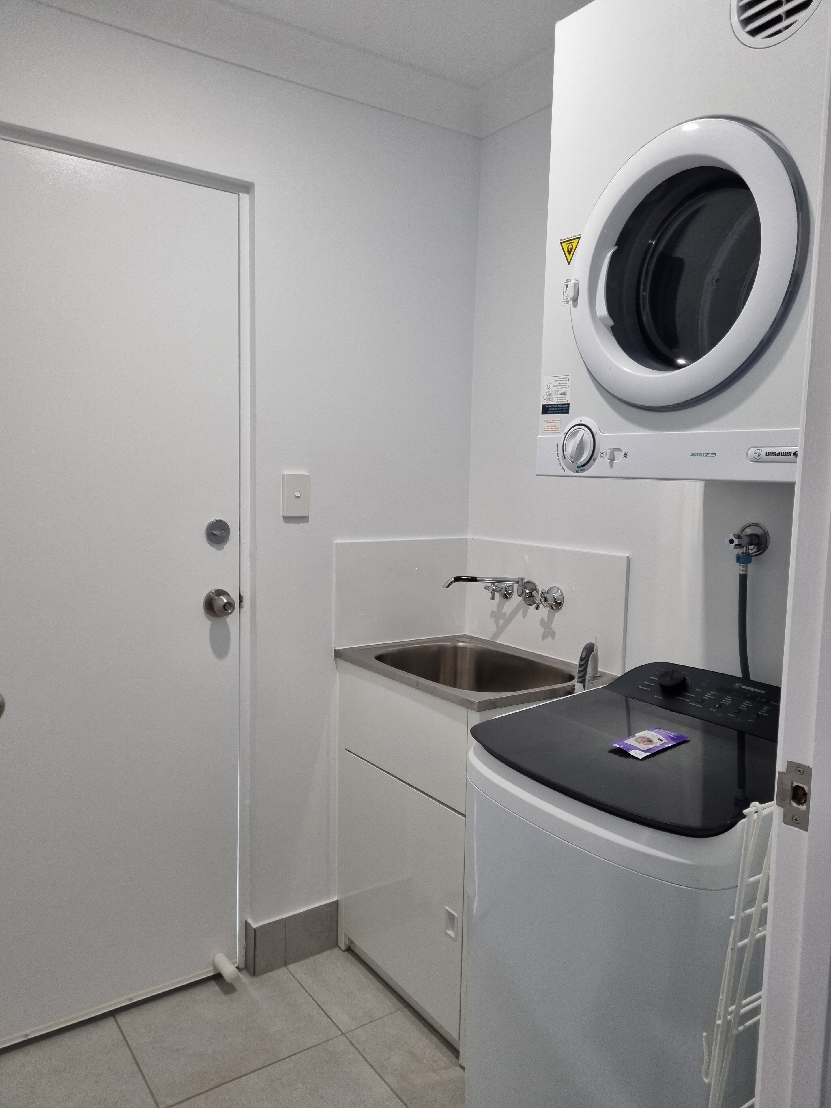 A compact laundry room with a front-loading washing machine, a sink, and a door.