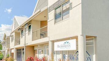 Ein mehrgeschossiges Gebäude mit einem Schild für Rockhampton Property Group. Es hat Balkone, einen verschlossenen Eingangsbereich und einen angelegten Vorgarten mit Sträuchern.