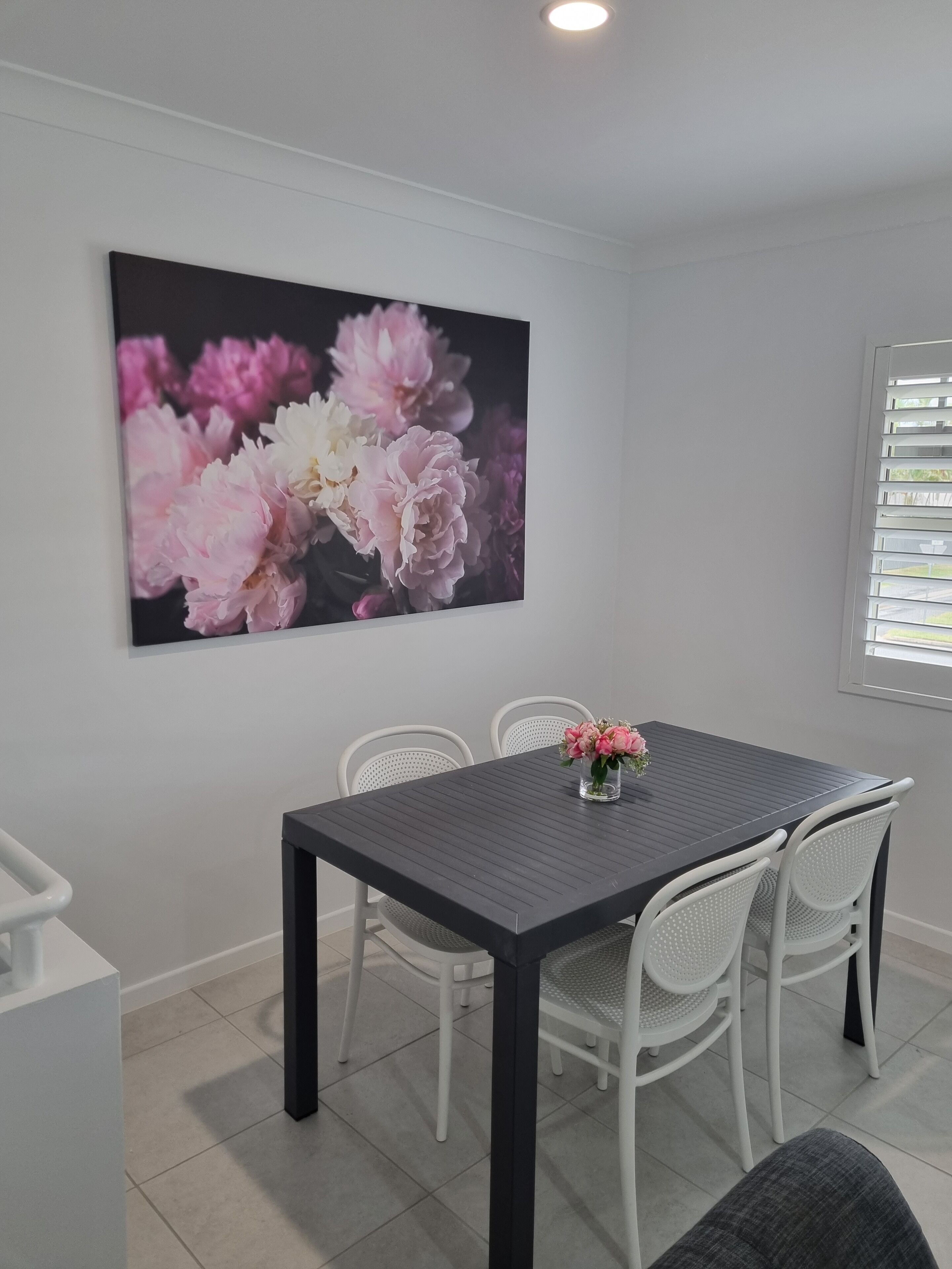A dining area with a dark table, white chairs, and a large floral artwork on the wall.