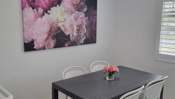 A dining area with a dark table, white chairs, and a large floral artwork on the wall.