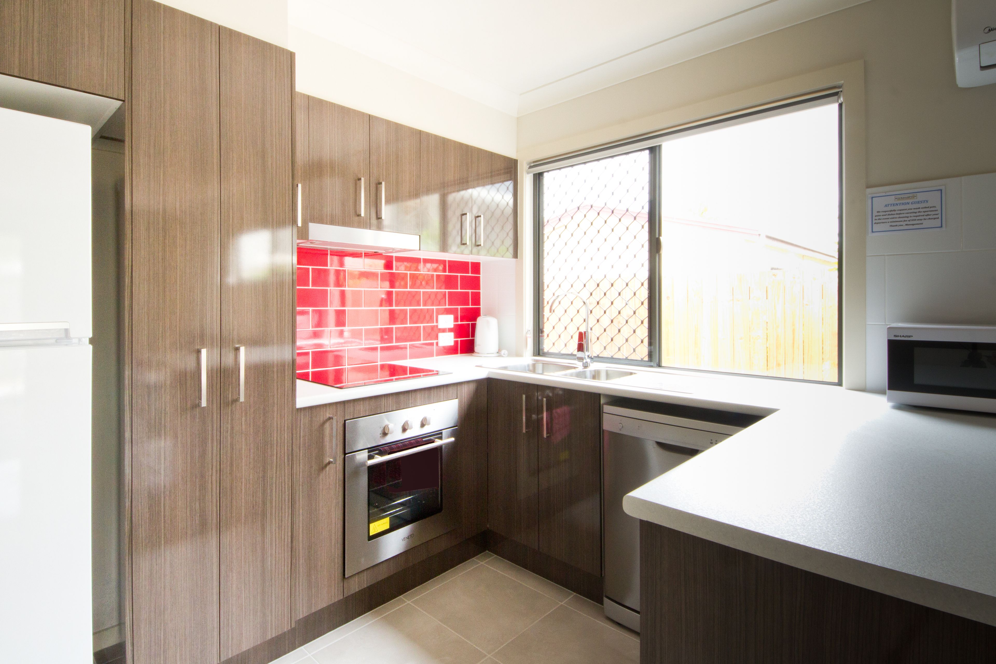 Une cuisine moderne avec des meubles en bois, un crédence rouge et une grande fenêtre.