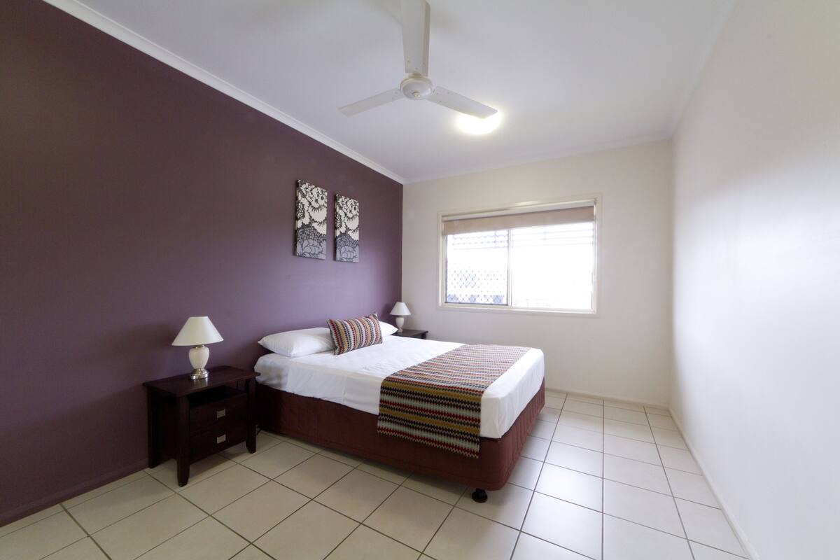 A bedroom with a bed, nightstands, a ceiling fan, and a window.