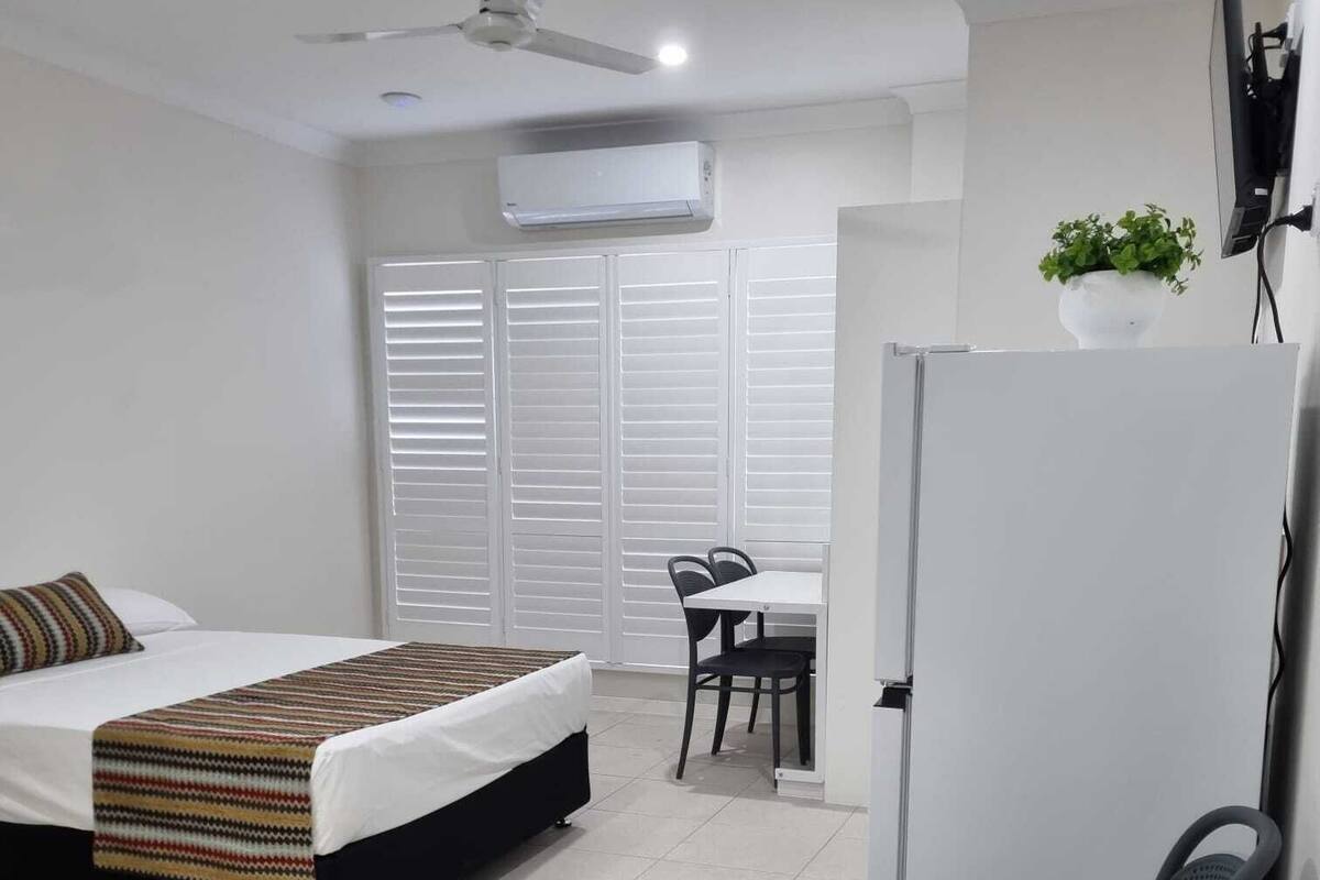 A compact hotel room with a bed, a desk, a chair, and a refrigerator.