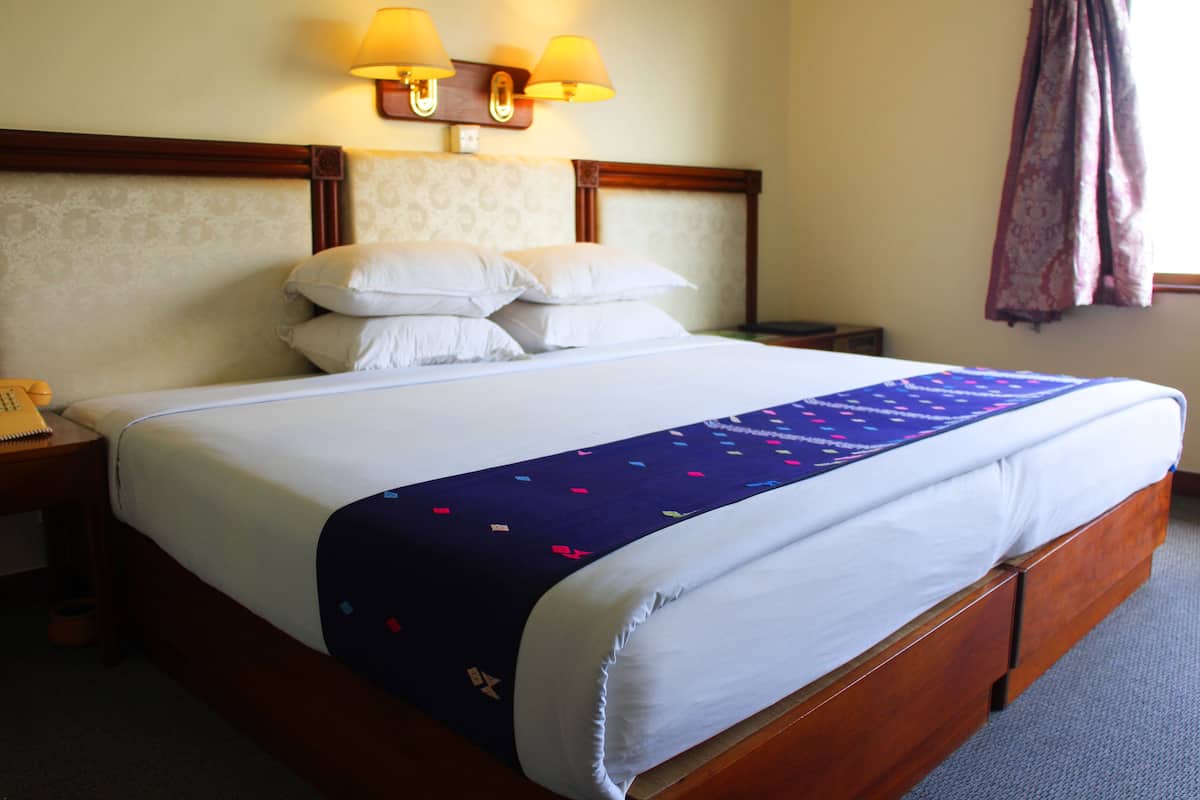 A hotel room with a large bed, a wooden headboard, two bedside lamps, a nightstand, and a telephone.