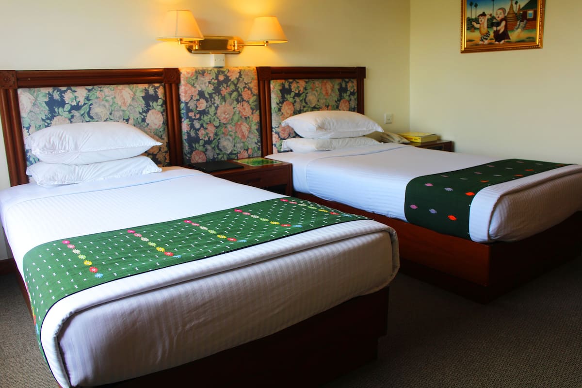 Two single beds with wooden headboards, a nightstand with a lamp, and a floral wallpaper.