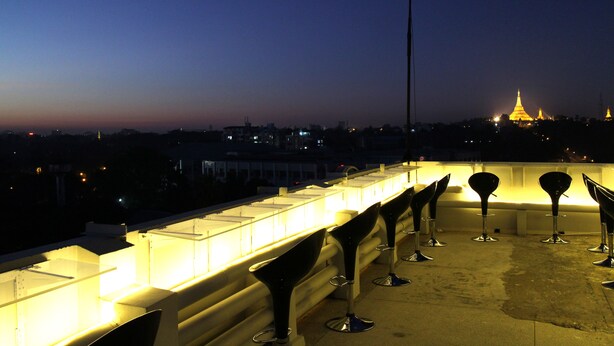 A rooftop terrace with modern bar stools and a cityscape view at dusk.