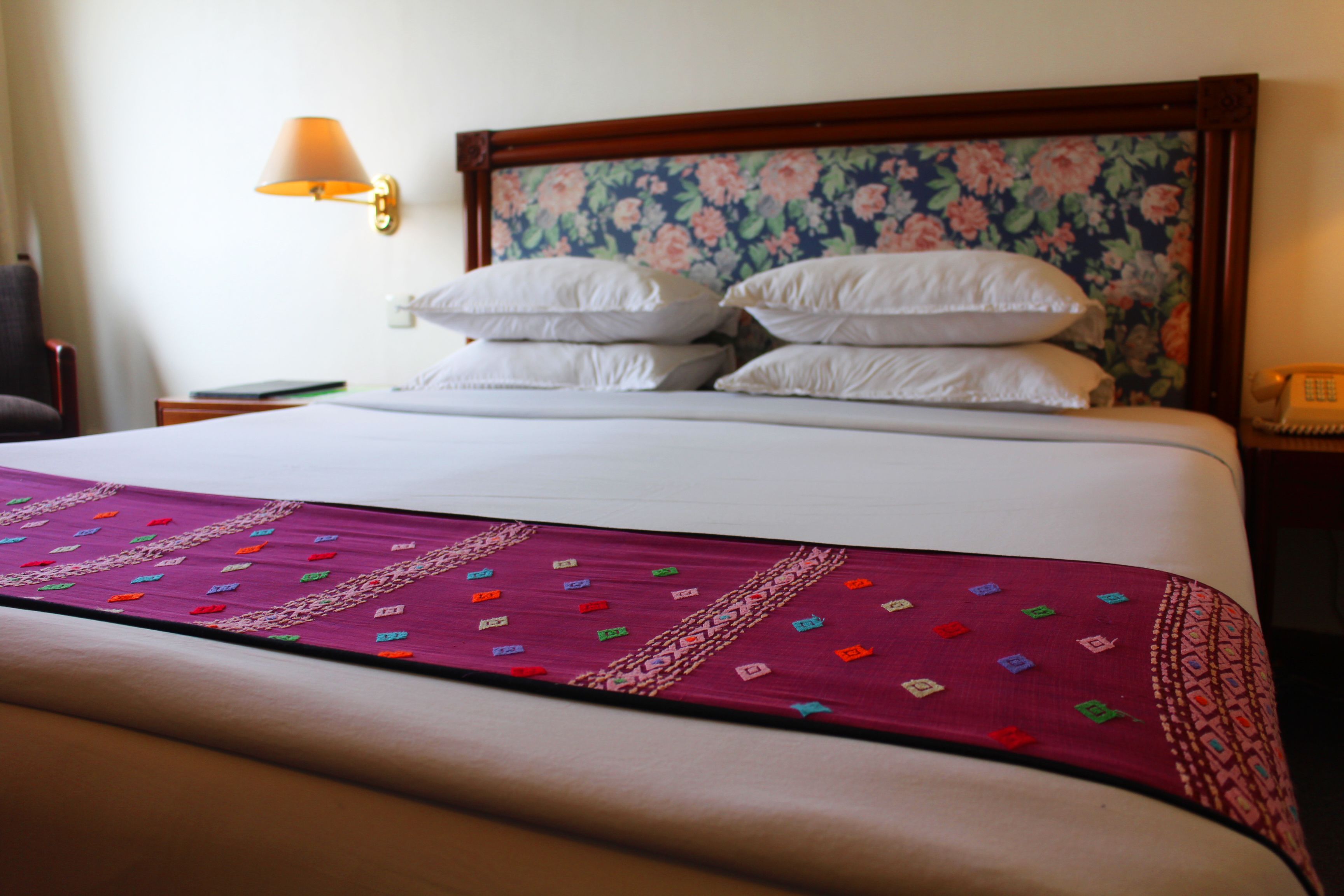 A neatly made bed with a floral headboard, a bedside lamp, and a telephone on the nightstand.