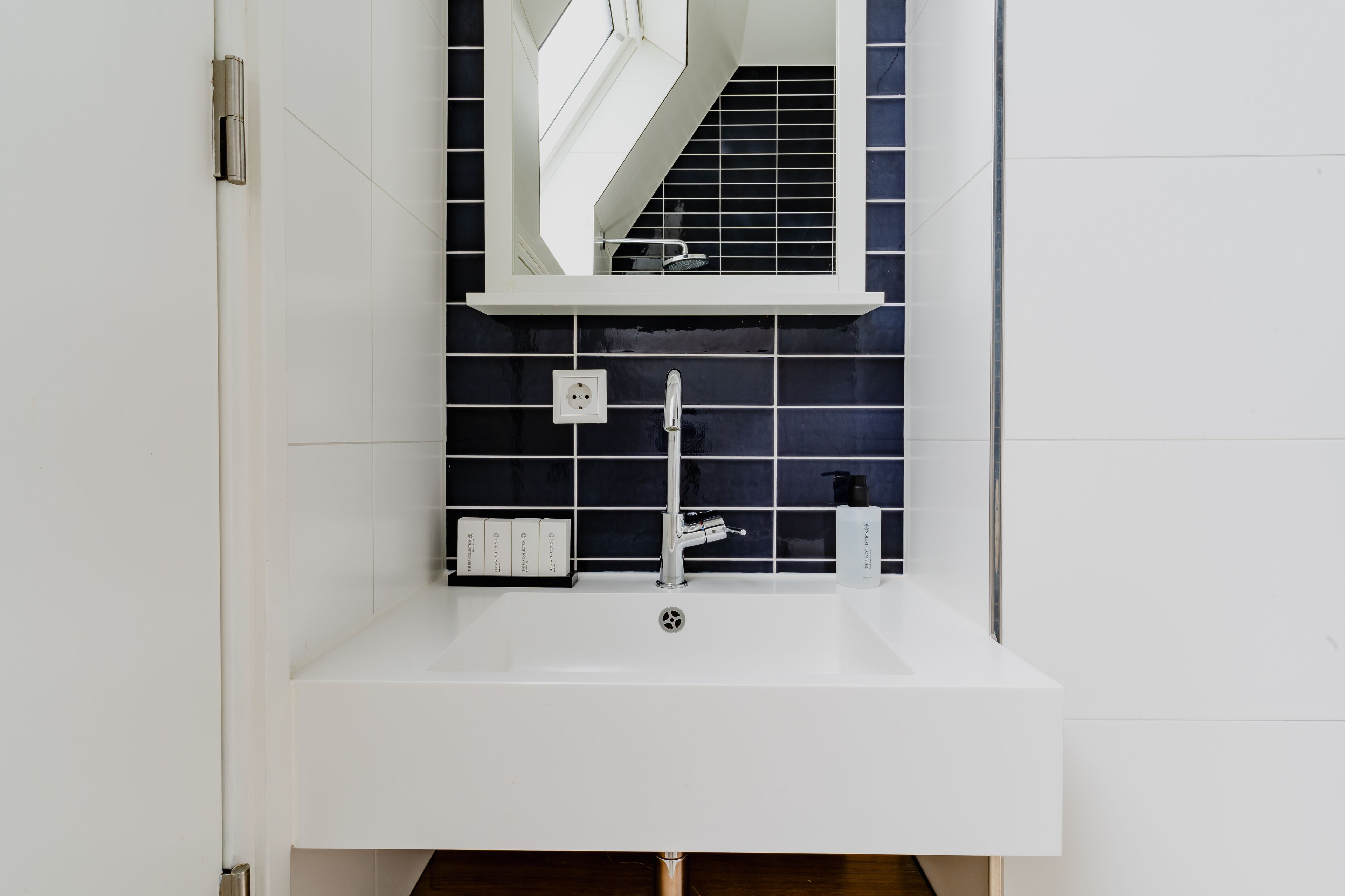 A modern bathroom with a white sink, a mirror, and a black tiled backsplash.