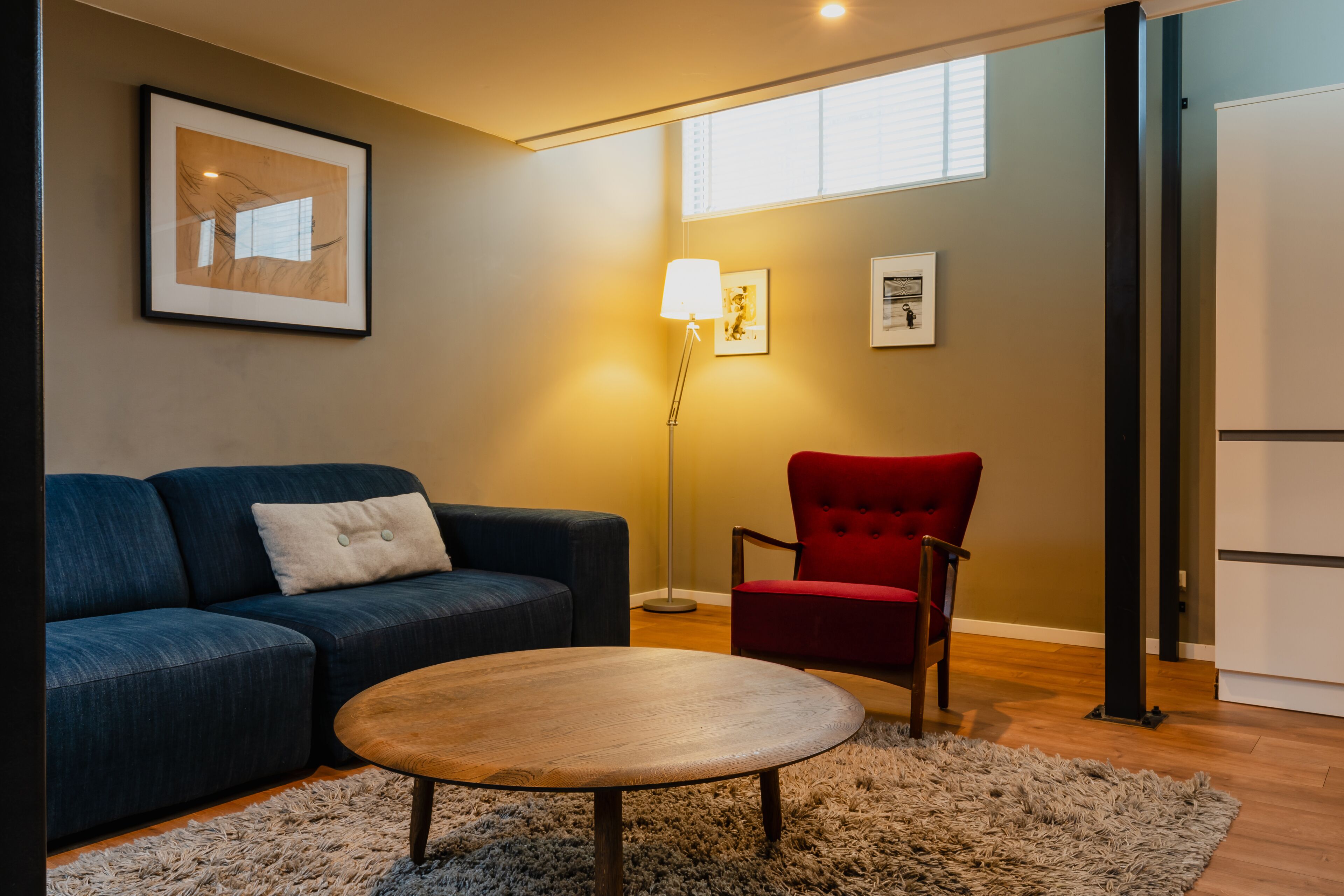 A living room with a blue sofa, a red armchair, a wooden coffee table, and a floor lamp.
