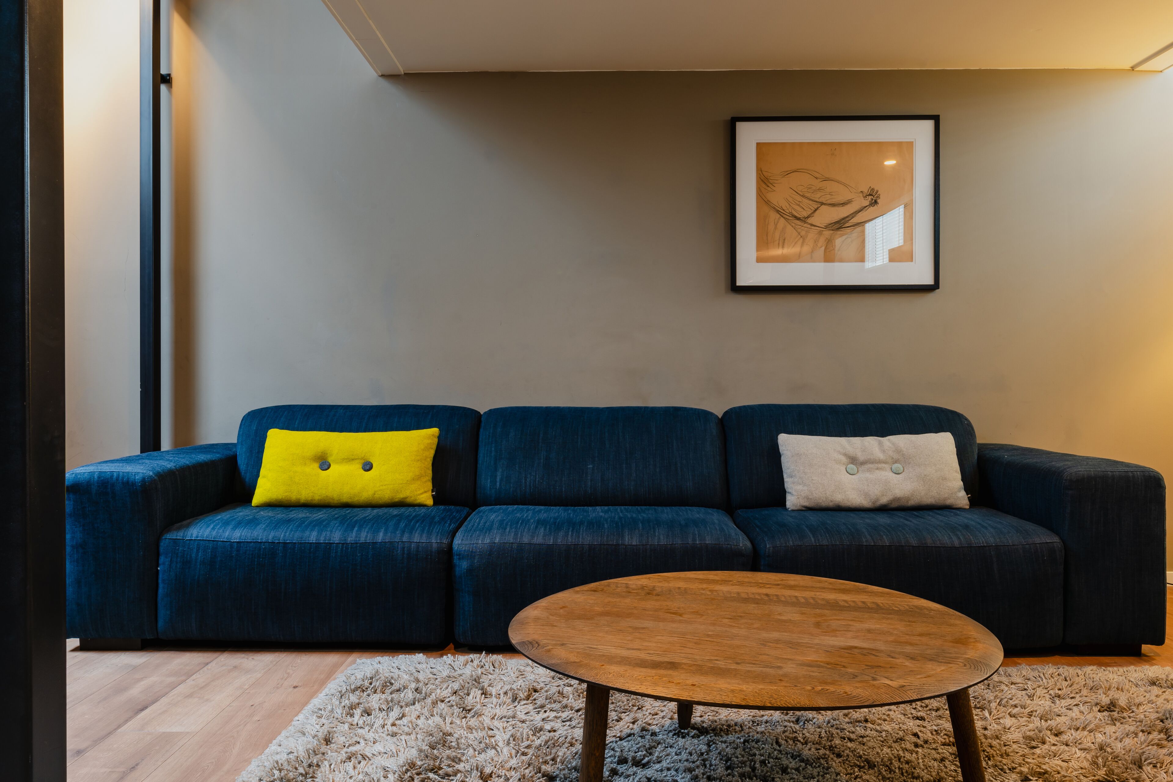 Una sala de estar moderna con un sofá azul oscuro, una mesa de centro de madera y una obra de arte enmarcada en la pared.