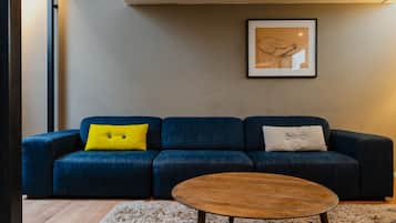 Una sala de estar moderna con un sofá azul oscuro, una mesa de centro de madera y una obra de arte enmarcada en la pared.