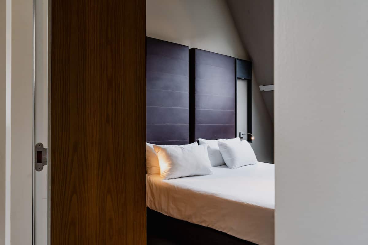 A modern bedroom with a large bed, dark headboard, and a wooden door.