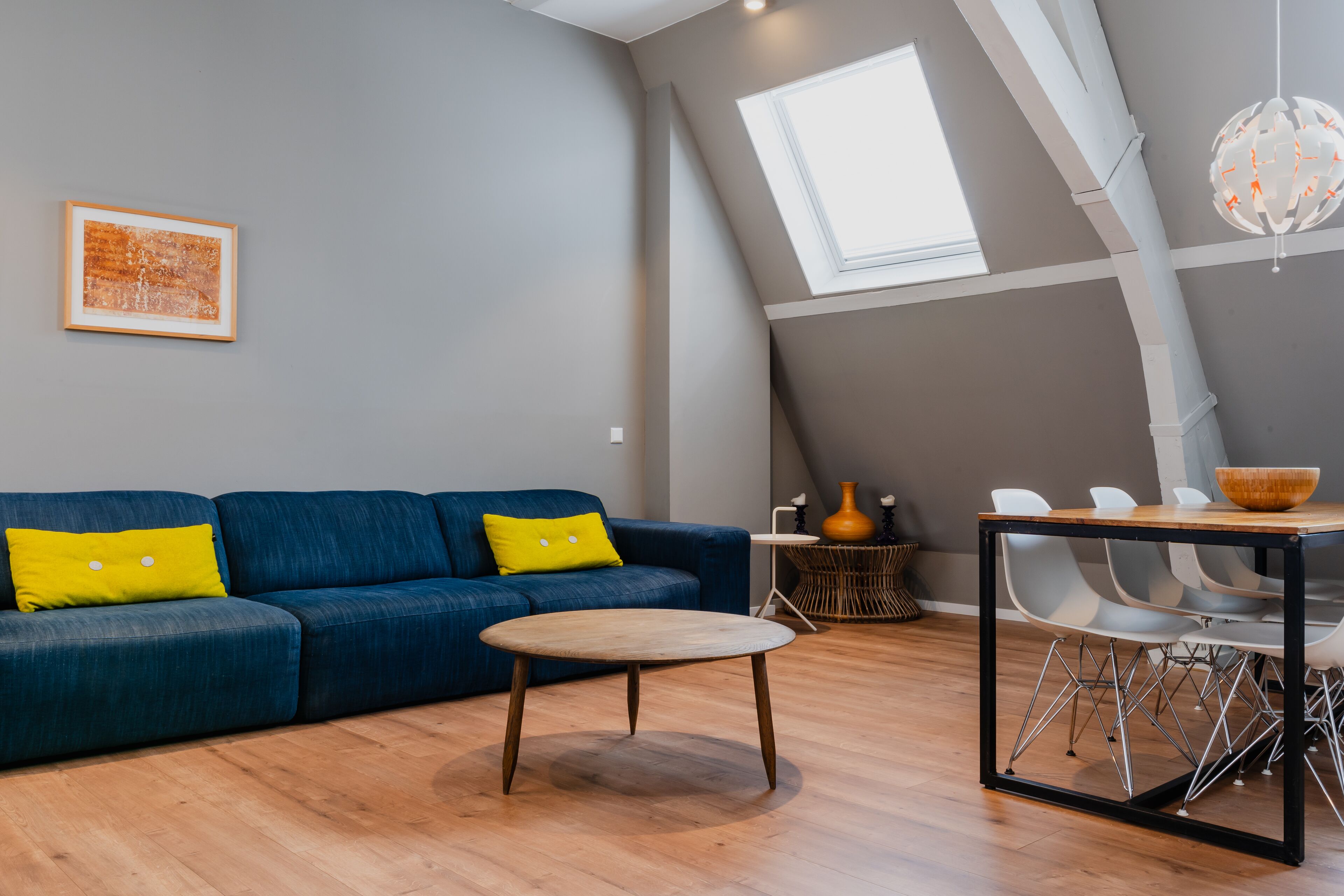 Una sala de estar moderna con un sofá azul, una mesita redonda y un comedor con sillas y una mesa.