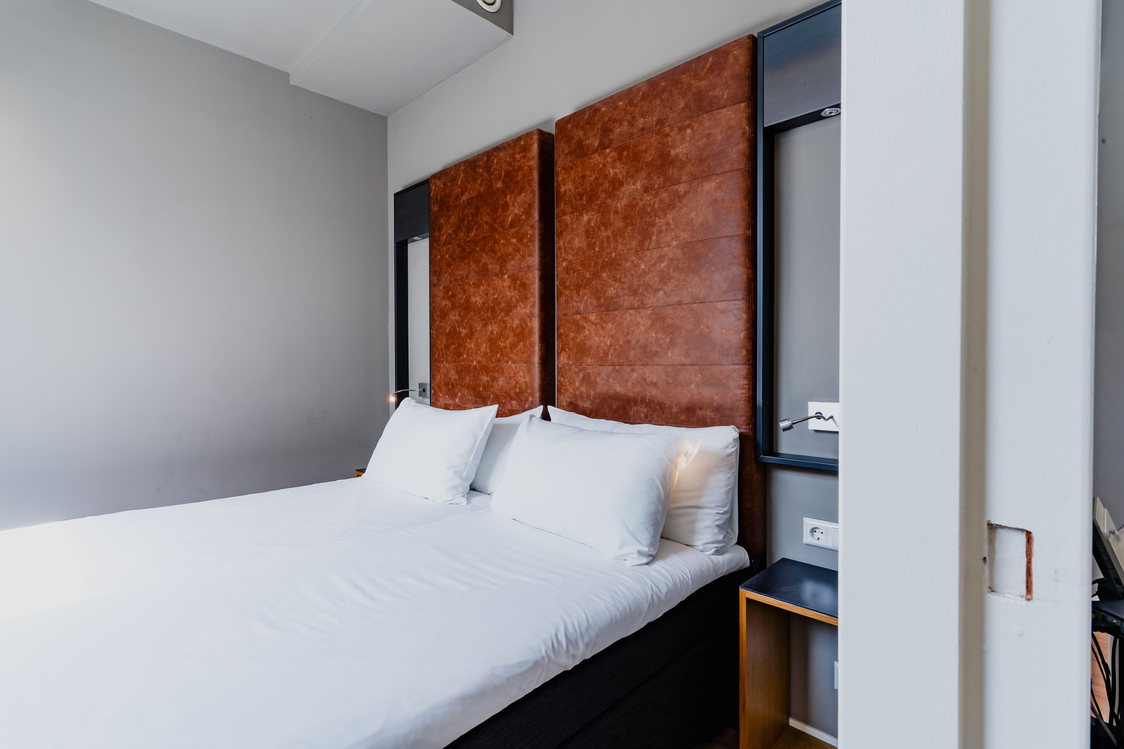A modern bedroom with a large bed, a wooden headboard, and a small bedside table.