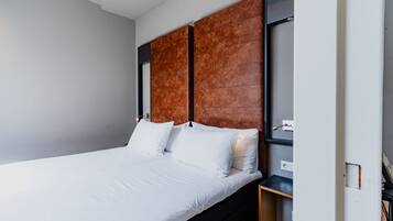 A modern bedroom with a large bed, a wooden headboard, and a small bedside table.