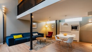 A modern living room with a blue sofa, a red chair, a round coffee table, and a dining area with a white table and chairs. - Apartments De Hallen (Amsterdam)