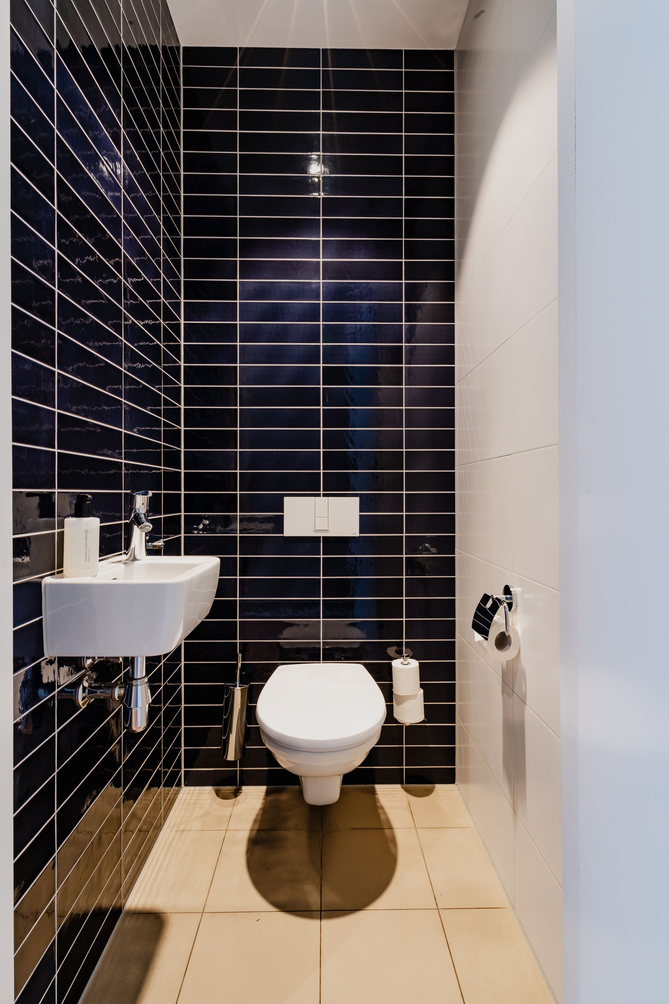 A modern bathroom with a black tiled wall, a white sink, and a toilet.
