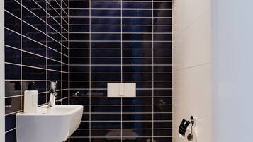A modern bathroom with a black tiled wall, a white sink, and a toilet.
