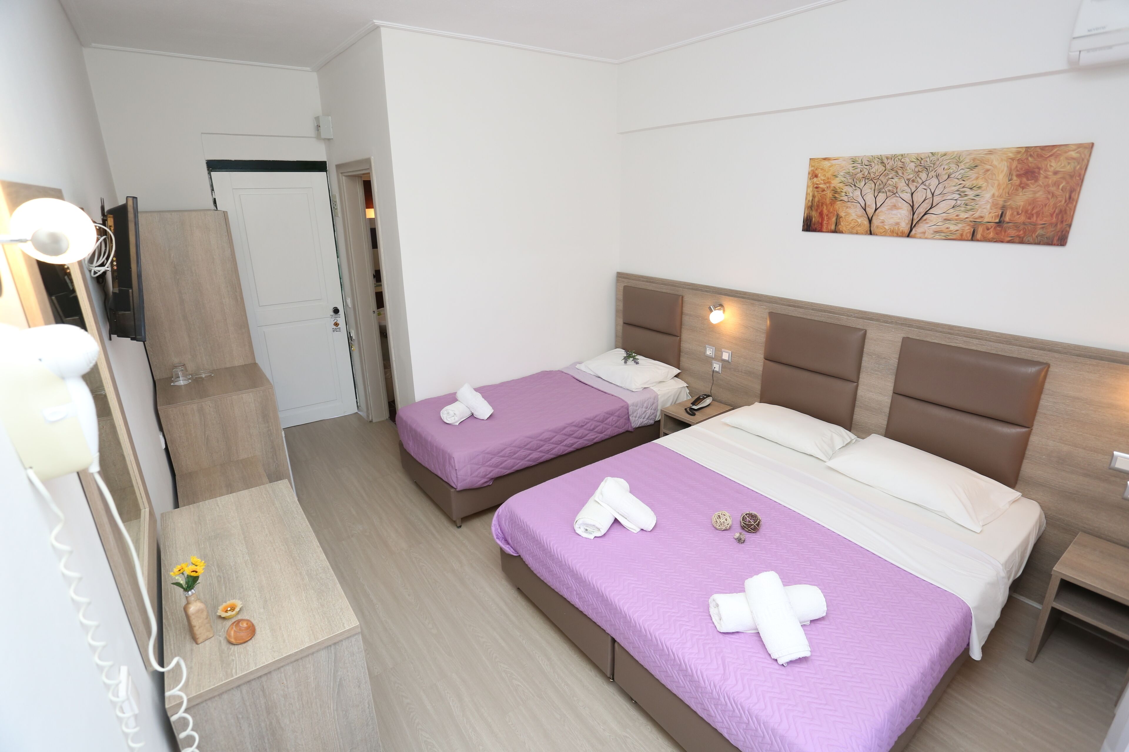 A hotel room with two beds, a wooden dresser, a vanity with a mirror, and a painting on the wall.