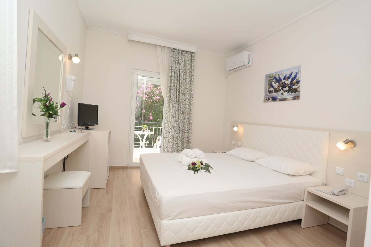 Una camera d'albergo con un letto, una scrivania, una sedia, una televisione, una finestra con tende e un quadro appeso al muro.
