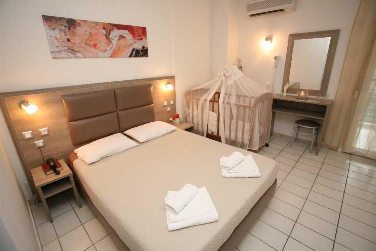 Camera d'albergo con un letto, comodino, abat-jour e un dipinto appeso al muro.
