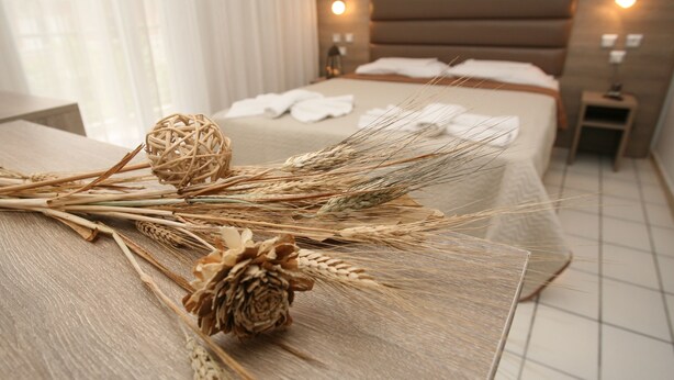 Un letto rifatto con lenzuola bianche e una testiera in legno, un comodino con una lampada e una finestra con tende leggere.