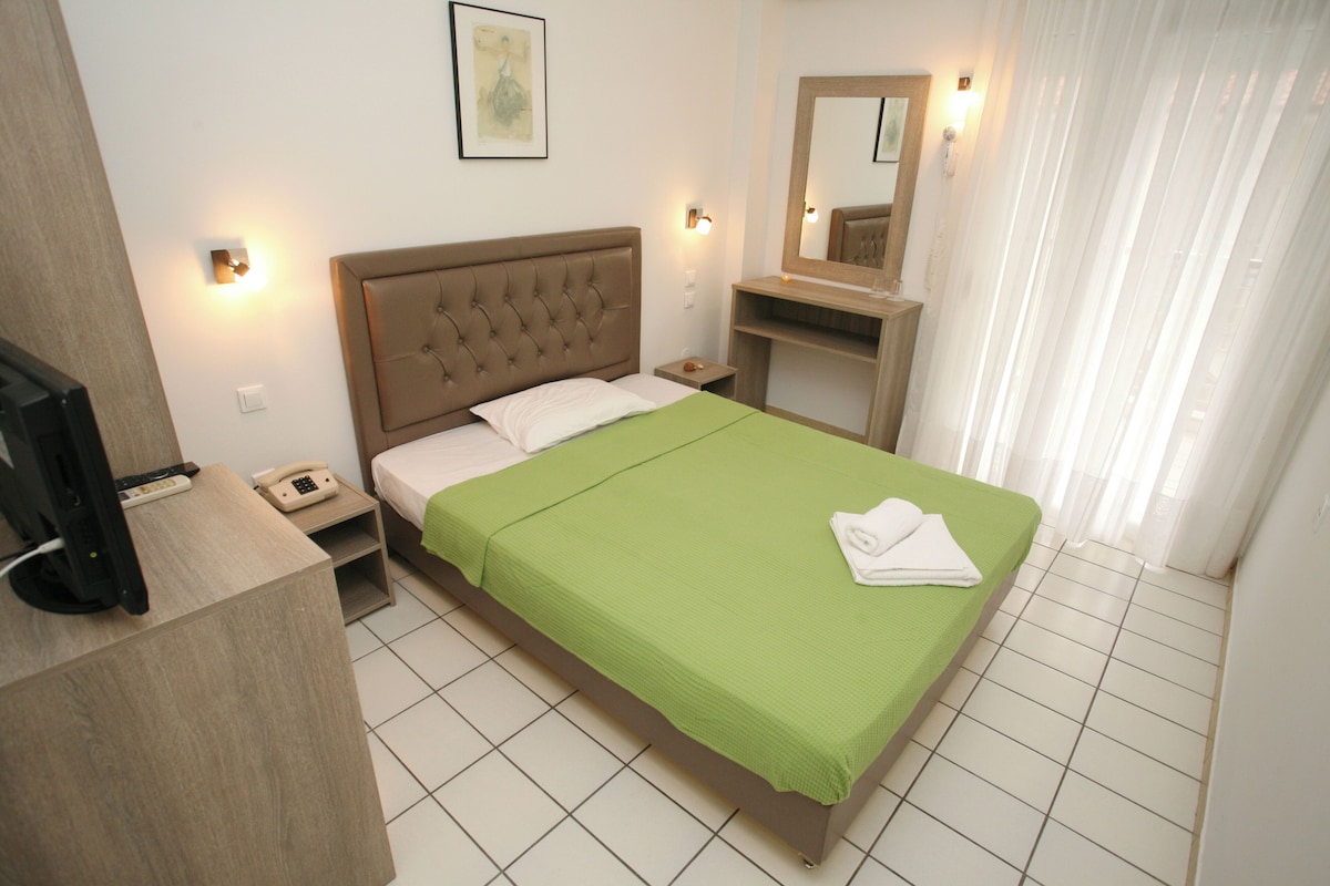 Una camera d'albergo con un letto, una scrivania con un telefono, uno specchio e una finestra con tende.