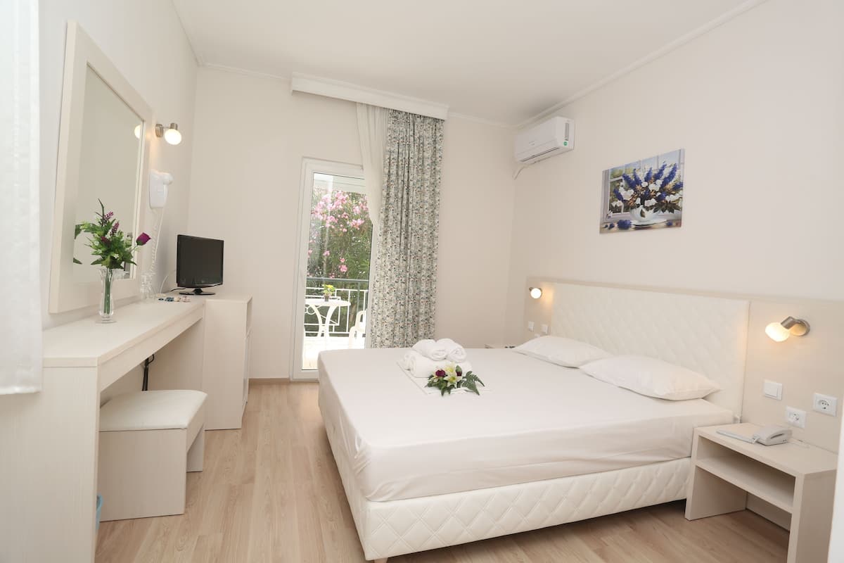 Una camera d'albergo con un letto, una scrivania, una sedia, una televisione, una finestra con tende e un quadro appeso al muro.
