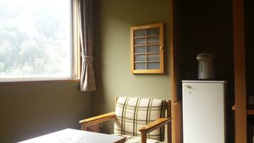 Una habitación pequeña con ventana, una silla, una mesa y un refrigerador.