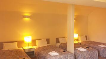 A hotel room with four single beds, each with a lamp and a remote control.