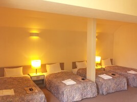 A hotel room with four single beds, each with a lamp and a remote control.