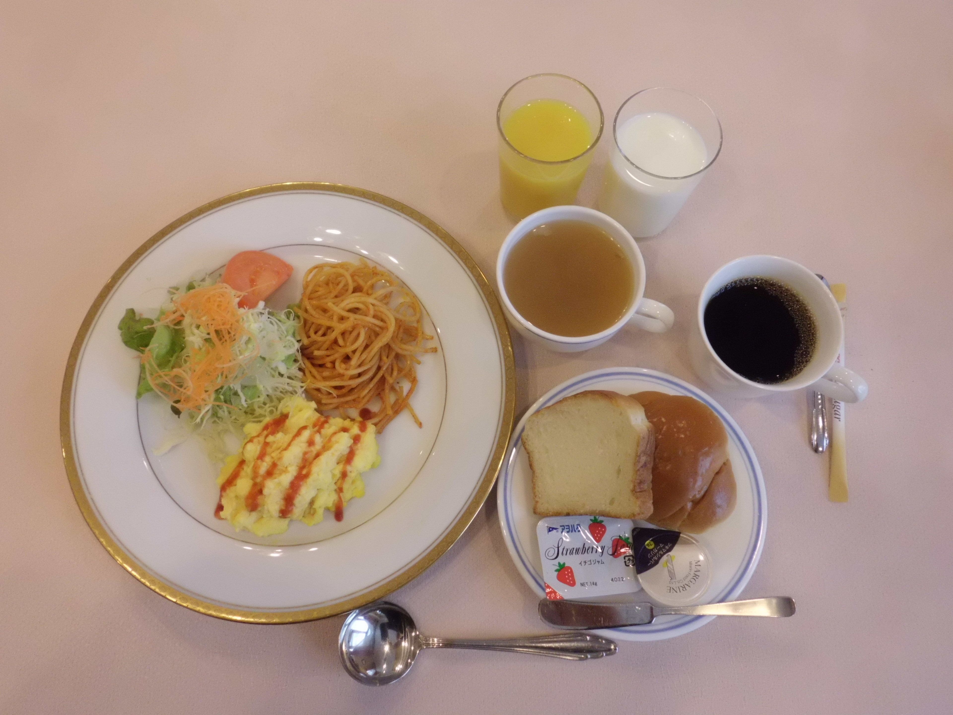A plate with spaghetti, salad, and toast, accompanied by two glasses of juice, a cup of tea, and a cup of coffee.