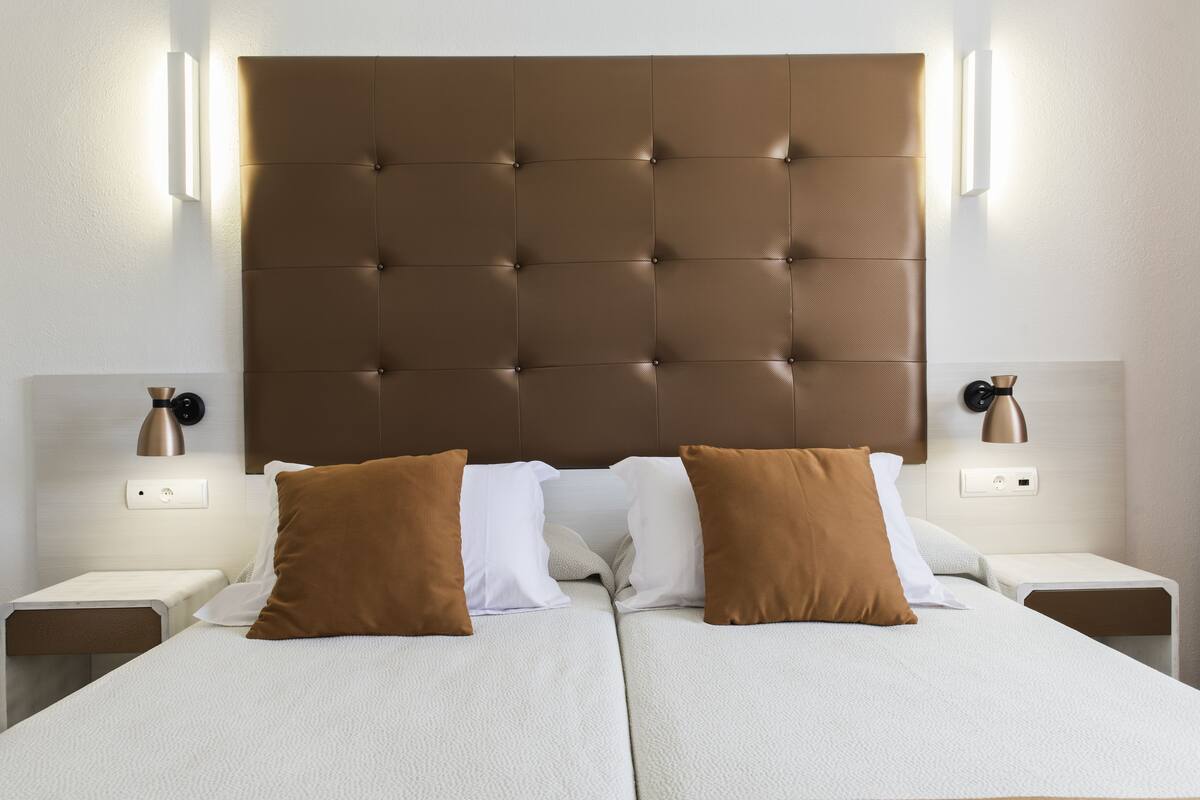 A double bed with a tufted headboard, two bedside tables with lamps, and a wall-mounted light fixture.