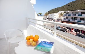 A balcony with a white chair, a bowl of fruit, and a book titled "IBIZA". - Oasis Sa Tanca Apartments by Typic Hotels (Santa Eulalia del Rio)