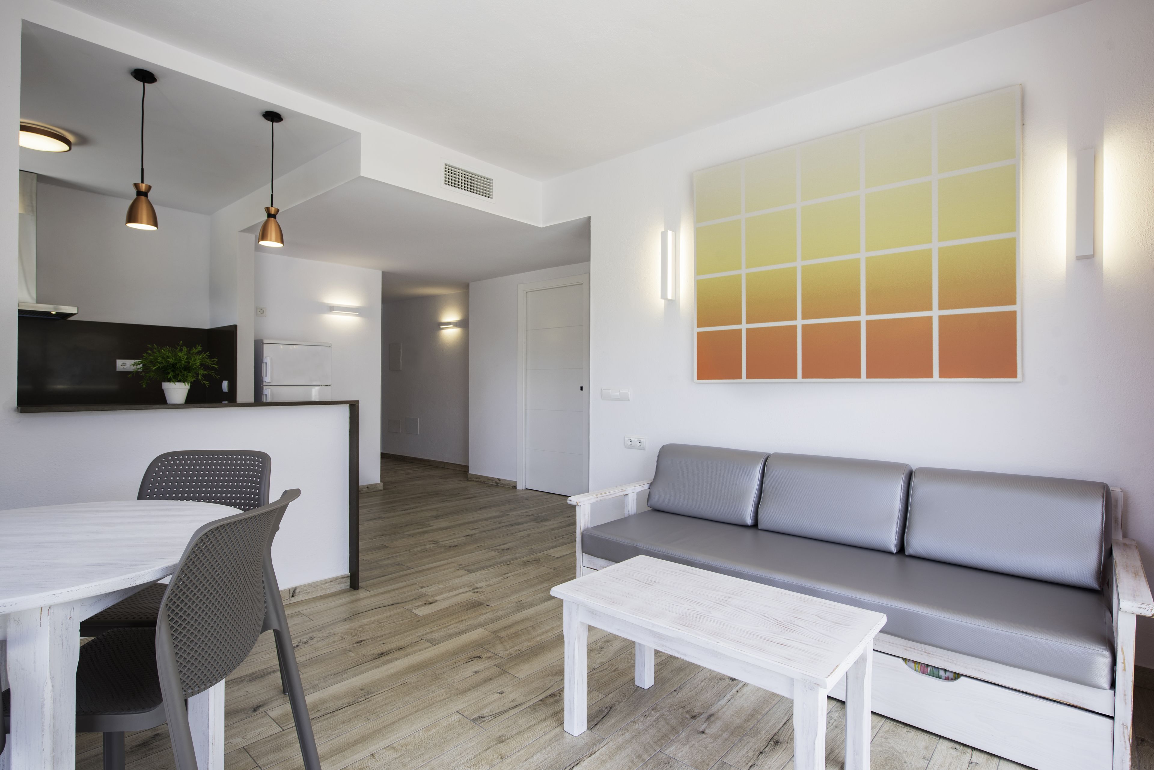Un salon moderne avec un canapé blanc, une table à manger avec des chaises et des luminaires suspendus.