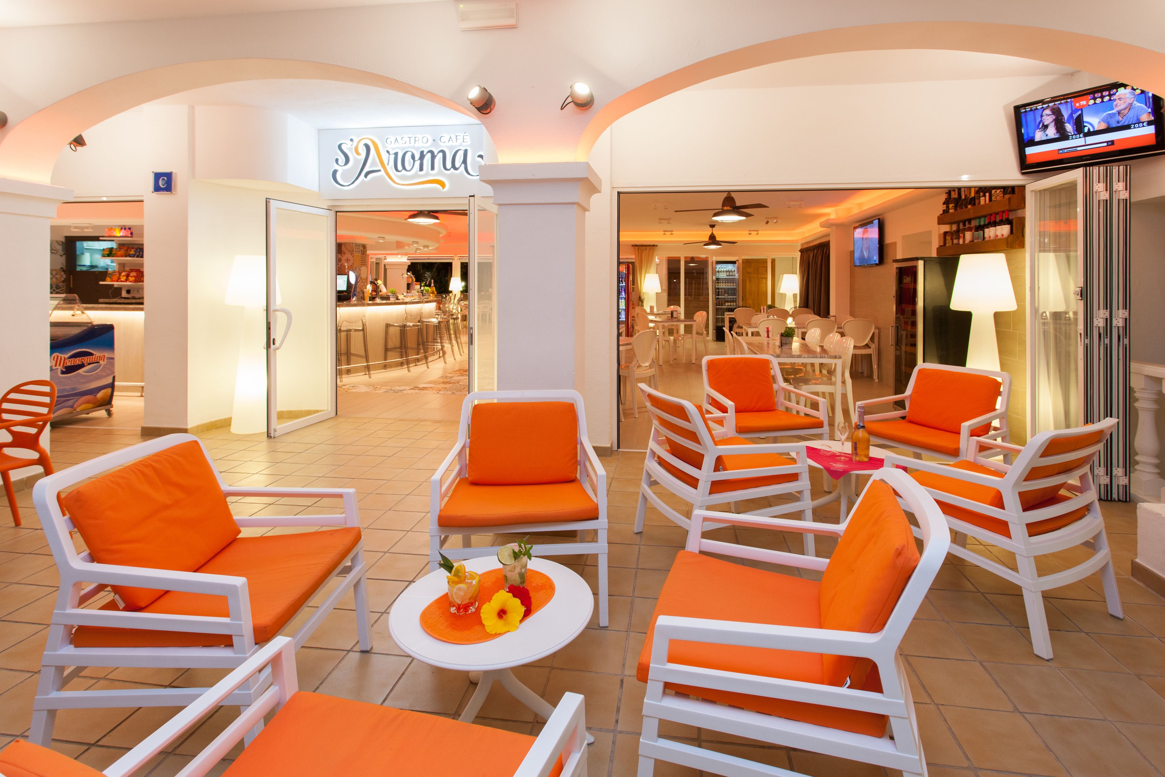 A hotel lobby with white chairs and orange cushions, a bar area, and a television screen.