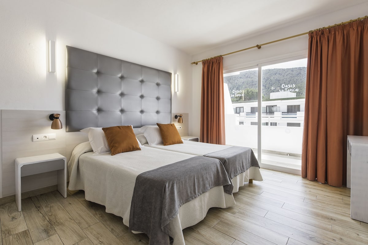 A modern hotel room with a large bed, two bedside tables, a flat-screen TV, and a view of the building outside.