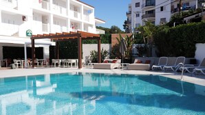 A clear swimming pool with lounge chairs and tables, surrounded by a white building with balconies. - Oasis Sa Tanca Apartments by Typic Hotels (Santa Eulalia del Rio)