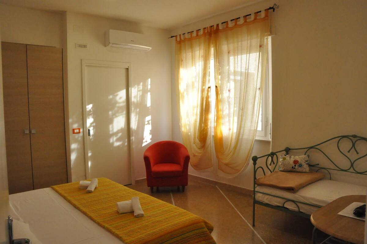 Una habitación de hotel con cama, una silla, un sofá, una ventana con cortinas y un armario.