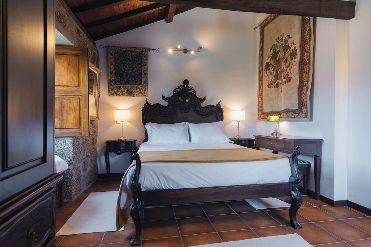 A bedroom with a large bed, wooden headboard, stone wall, and a tapestry.