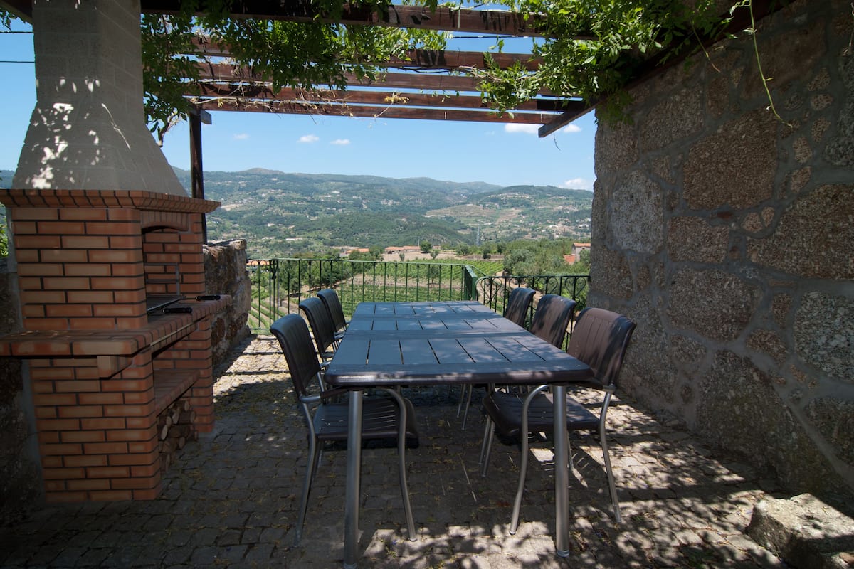 An outdoor patio with a brick barbecue, metal chairs, and a table.