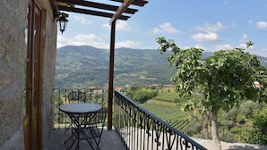 Un balcón con mesa y sillas, una pérgola y vistas a un viñedo y montañas.