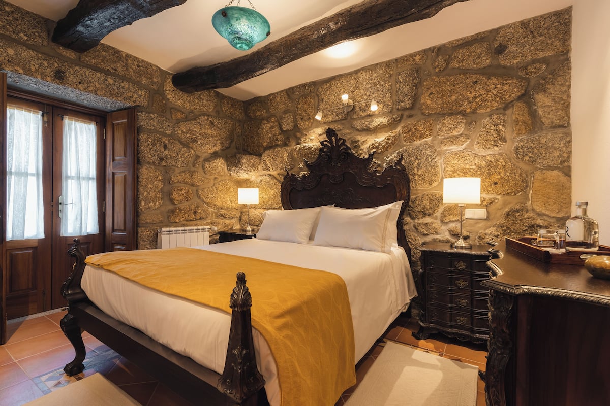 A stone-walled bedroom with a large bed, wooden headboard, and two bedside lamps.