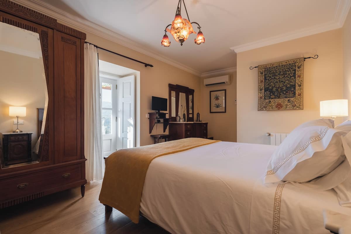 A well-lit bedroom with a large bed, a wooden dresser, a mirror, and a chandelier.