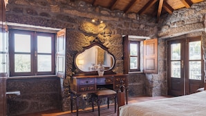 Un dormitorio rústico con paredes de piedra, un aparador de madera, un espejo grande y una cama.