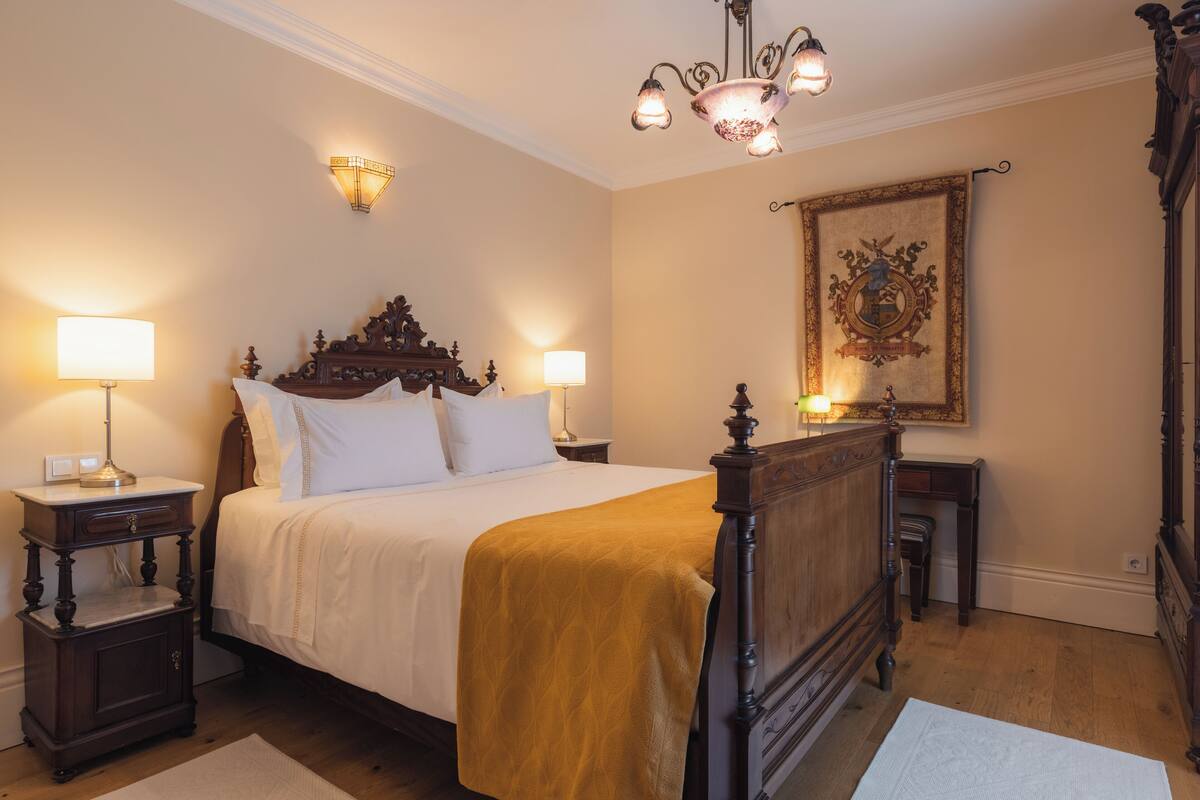 A bedroom with a large bed, two bedside tables, a chandelier, and a decorative wall piece.